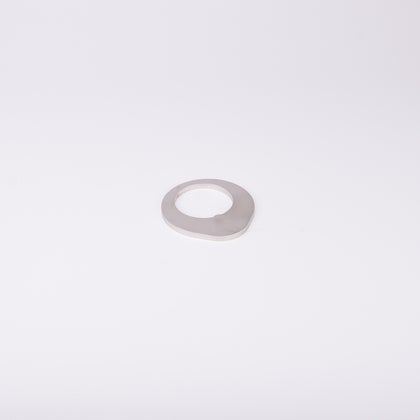 Distansbricka i metall med oregelbunden form och ett centralt hål.