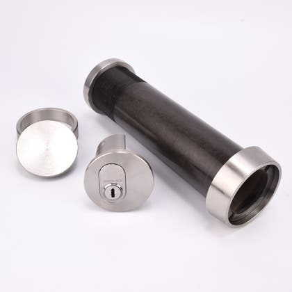 Cylindrisk nyckelfacksrör med svart kropp och silverfärgade ändar, samt ett runt lås och en rund bricka.