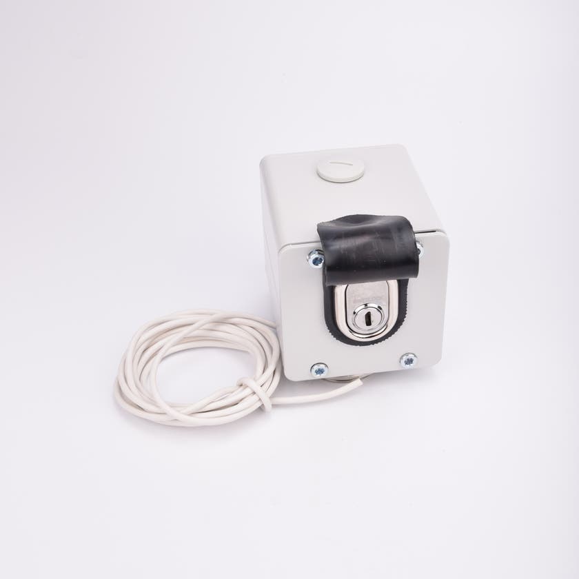 Vit kubformad nyckelbrytare med en nyckelcylinder som syns under ett svart lock, samt tillhörande vit kabel ihoprullad intill.