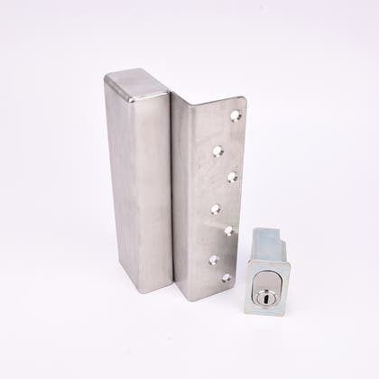 Två metallföremål visas. Det större är en L-formad nyckelförvaringsenhet med flera cirkulära hål längs ena sidan. Det mindre är en rektangulär cylinderhållare med en oval cylinder.