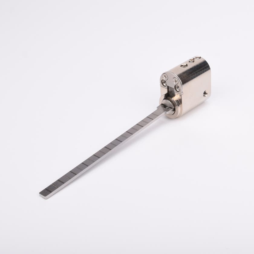 Oval låscylinder i silverfärgad metall med en lång, platt, räfflad metall medbringare.