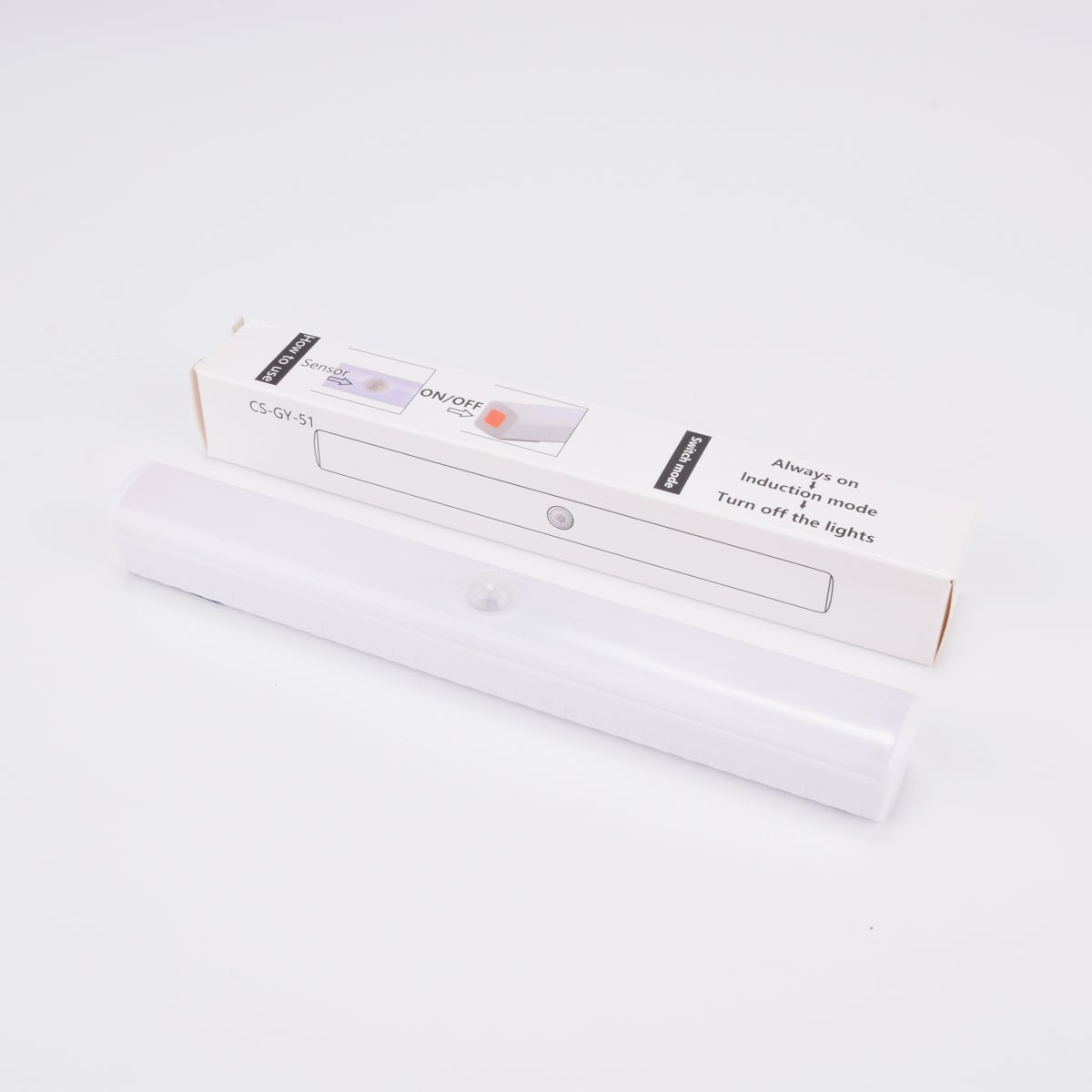 Vit LED-lampa med rörelsesensor, liggande framför sin förpackning.