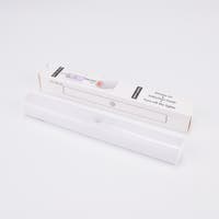 Vit LED-lampa med rörelsesensor, liggande framför sin förpackning.