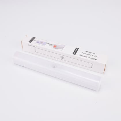 Vit LED-lampa med rörelsesensor, liggande framför sin förpackning.