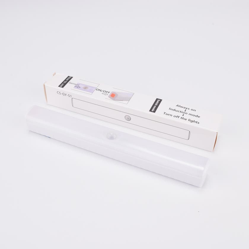 Vit LED-lampa med rörelsesensor, liggande framför sin förpackning.