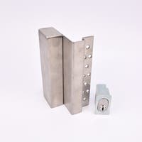 Två metallföremål visas. Det större är en L-formad nyckelförvaringsenhet med flera cirkulära hål längs ena sidan. Det mindre är en rektangulär cylinderhållare med en oval cylinder.