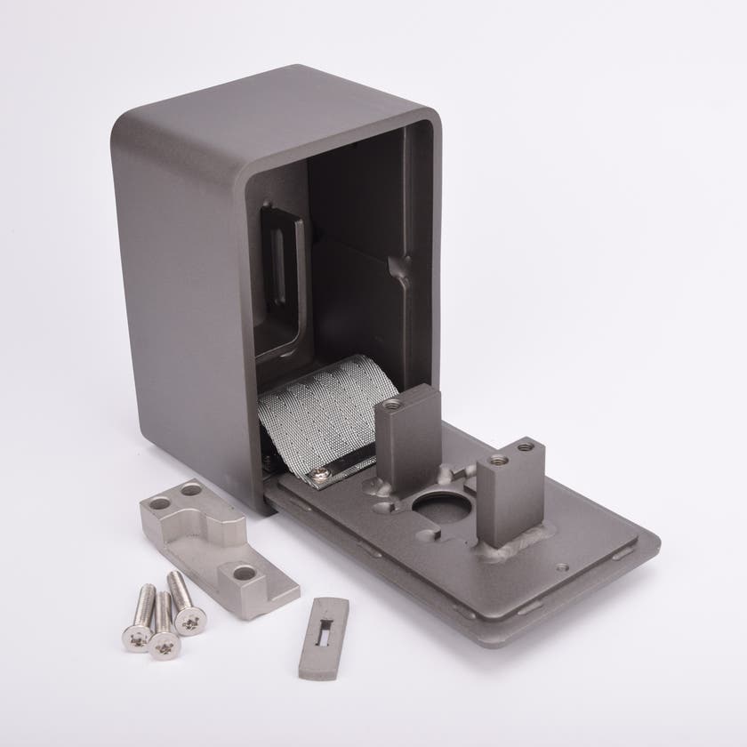 Grått fasadnyckelskåp i metall med rundade hörn och helt utfälld lucka, samt metallkomponenter och skruvar liggandes utanför.