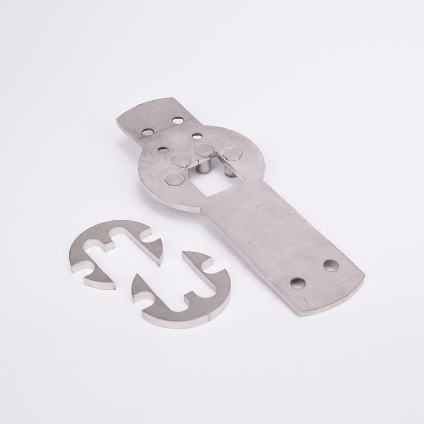 Tre metallkomponenter: en rektangulär platta med hål och utskärningar samt två halvcirkelformade delar med krokformade utskärningar.