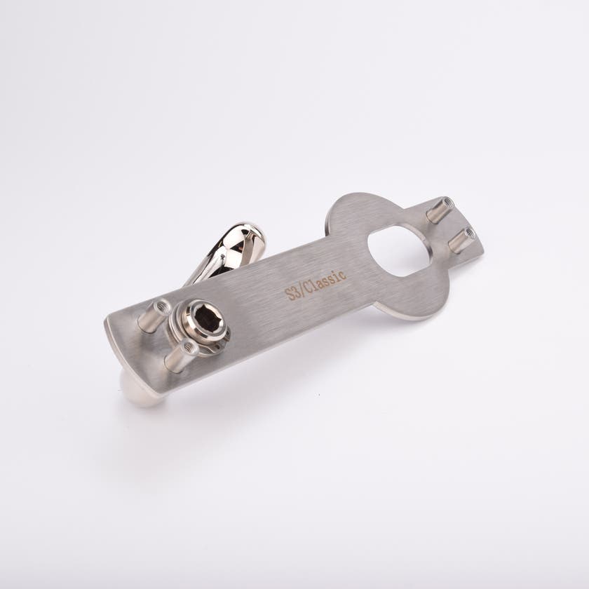 Blankt metallhandtag monterat på rektangulär platta med två skruvhål och ett ovalt hål.