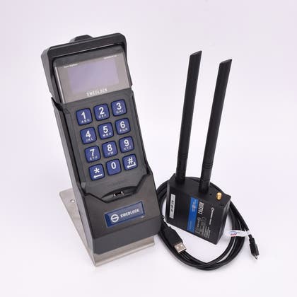 En synkstation med elektronisk knappsats med display, bredvid en svart låda med två antenner och en svart ihoprullad kabel.