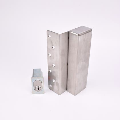 Två metallföremål visas. Det större är en L-formad nyckelförvaringsenhet med flera cirkulära hål längs ena sidan. Det mindre är en rektangulär cylinderhållare med en oval cylinder.