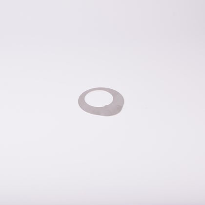 Distansbricka i metall med oregelbunden form och ett centralt hål.