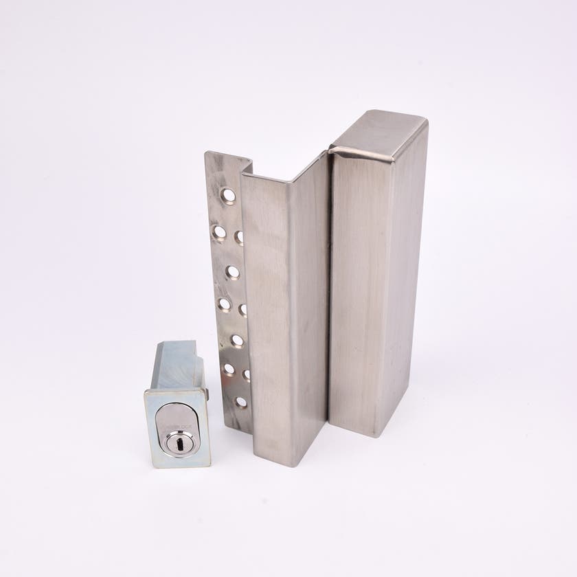 Två metallföremål visas. Det större är en L-formad nyckelförvaringsenhet med flera cirkulära hål längs ena sidan. Det mindre är en rektangulär cylinderhållare med en oval cylinder.