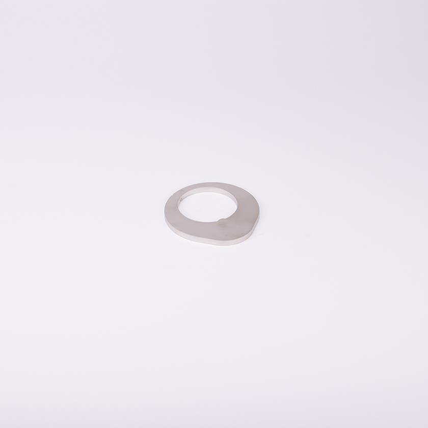 Distansbricka i metall med oregelbunden form och ett centralt hål.