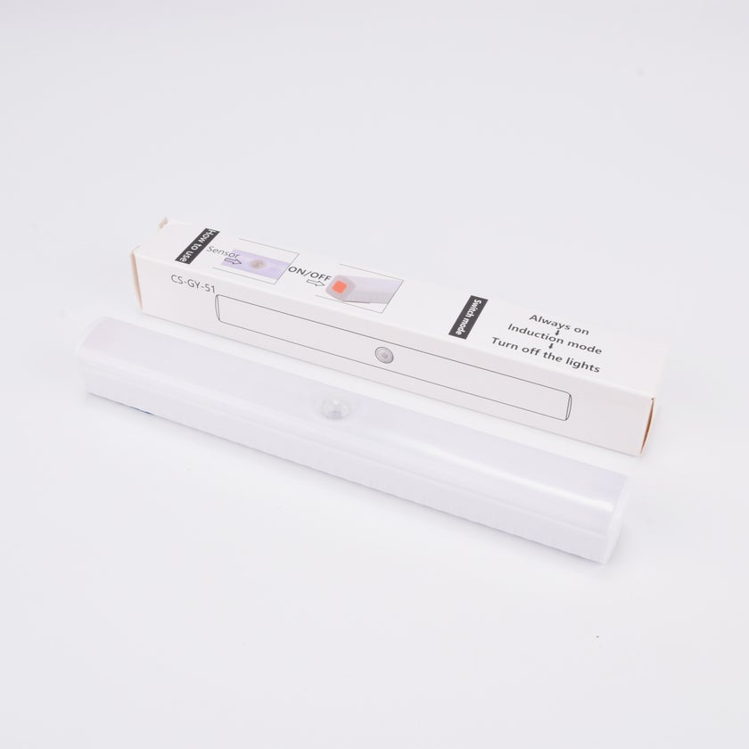 Vit LED-lampa med rörelsesensor, liggande framför sin förpackning.