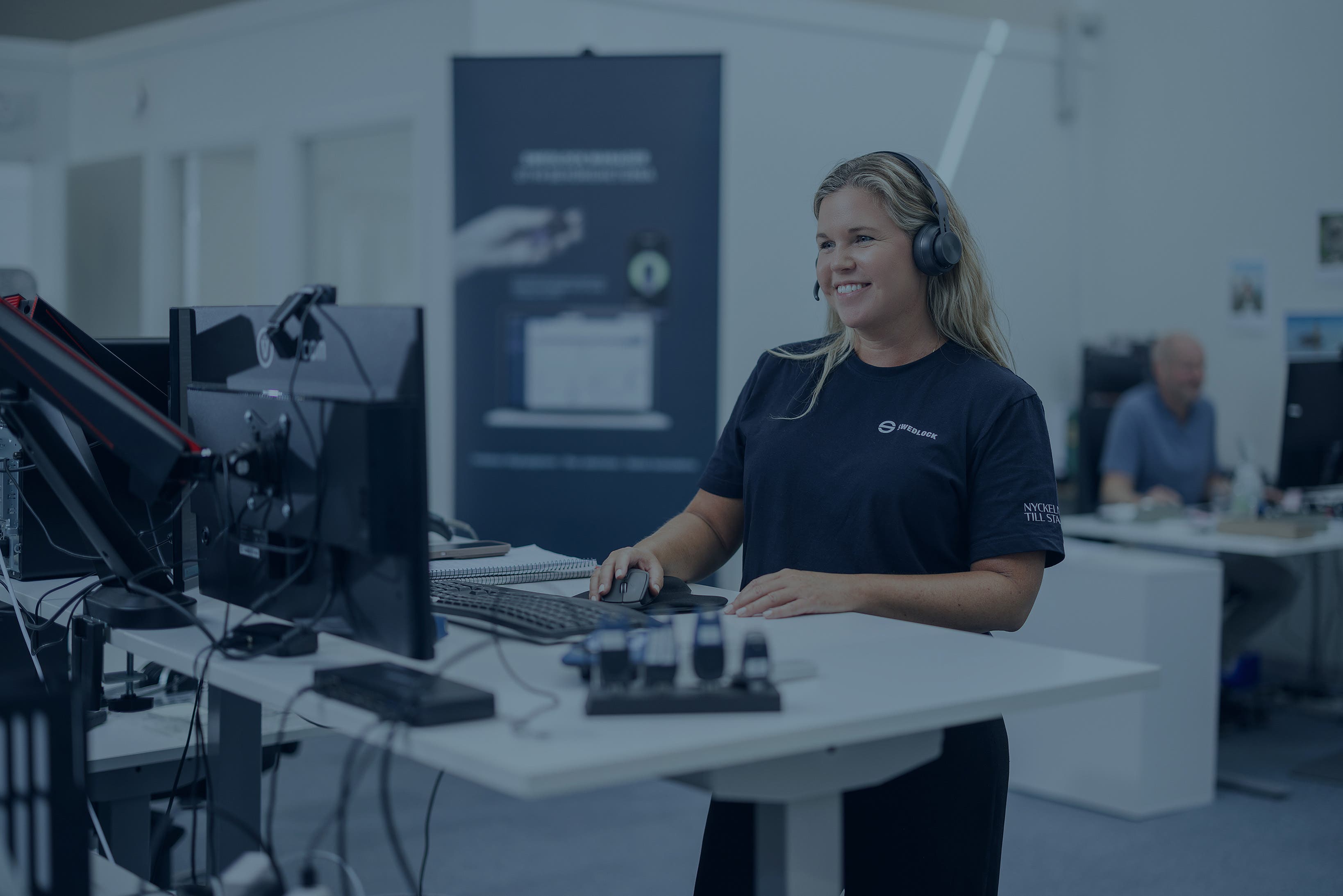To kvinner som står ved et skrivebord, i forgrunnen er et ikon for et par hodetelefoner