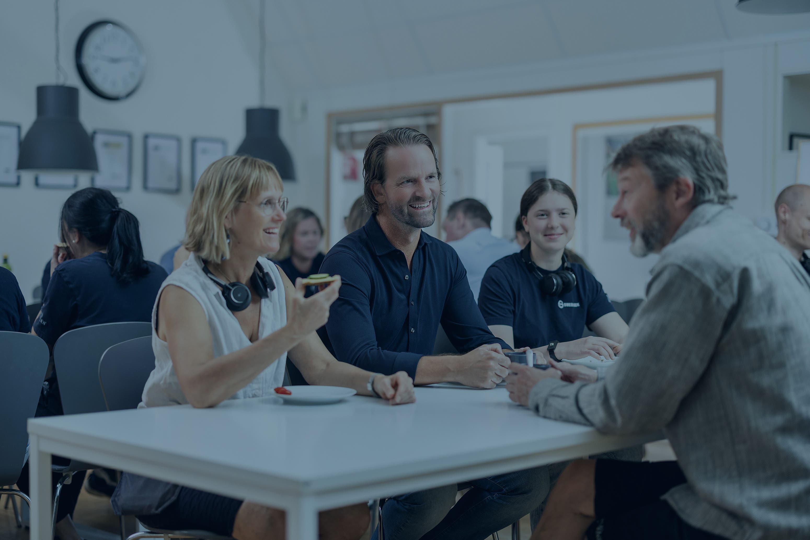 En grupp leende människor runt ett bord i ett lunchrum